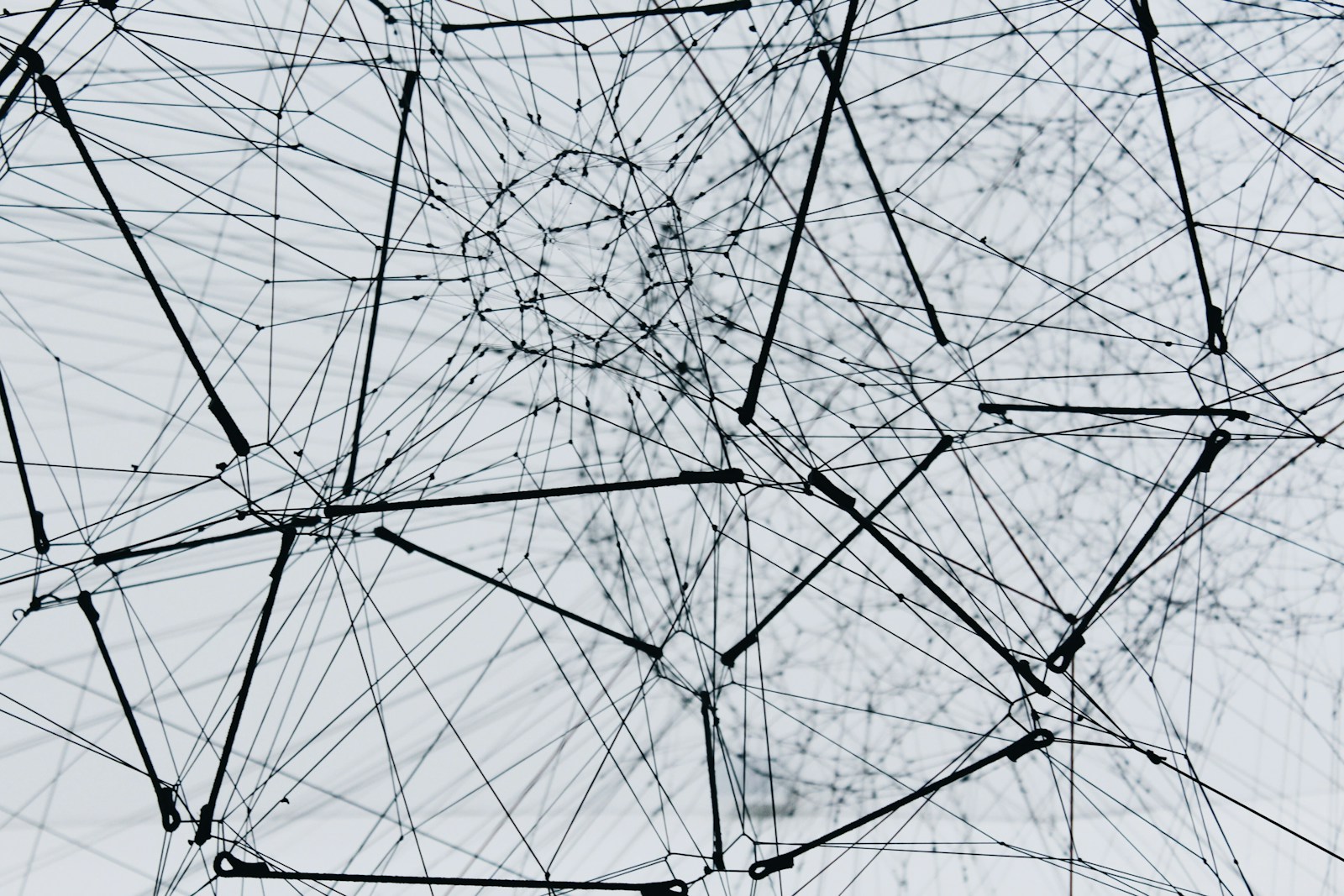 Tangled network of black wires and cables crisscrossing in front of a pale background, forming a chaotic web-like structure.